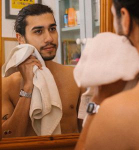 man drying face with towel while looking in the mirror