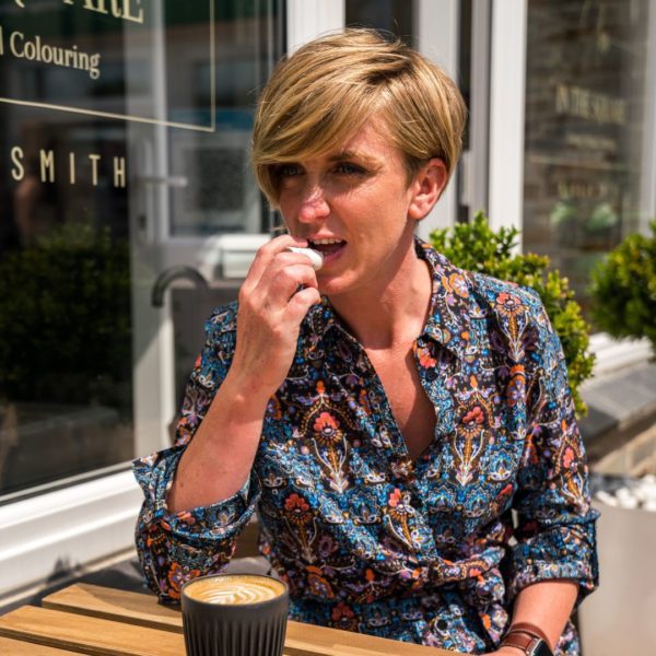 woman putting on lip balm sat outside a cafe