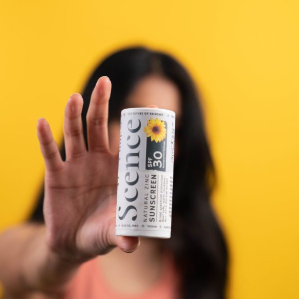 woman holding natural zinc sunscreen with bright yellow background